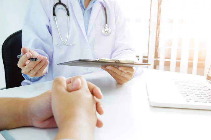 A doctor writing something and the patient with their hands folded