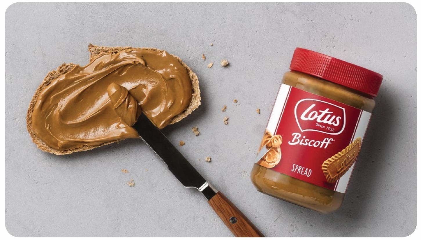 Biscoff spread being applied onto bread next to the bottle of the spread