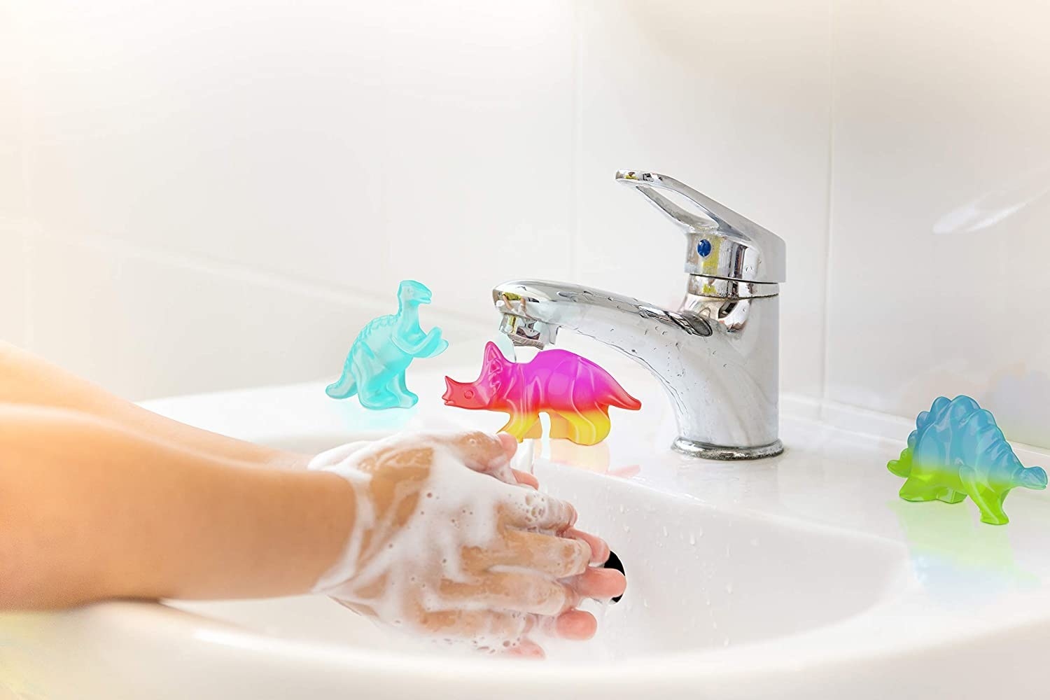 A person washing their hand in a sink with dino soaps around the edge