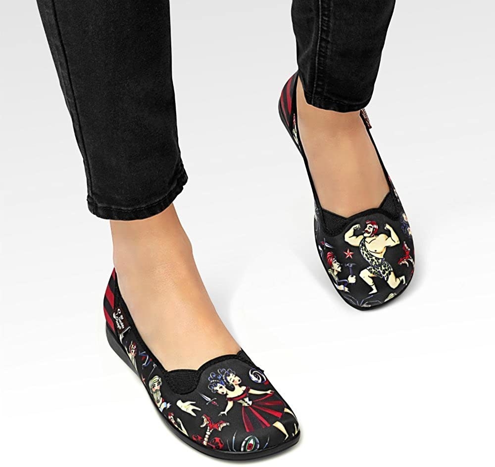 black round toe flats with a circus theme. the front of one shoe has a two headed lady and the front of the other shoe has a strong man.
