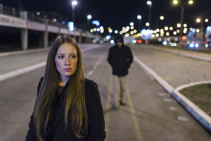 A woman being followed by a man on the street at night
