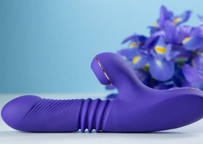 Purple thrusting rabbit vibrator next to purple flowers