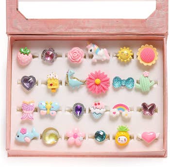 A pink box with 24 rings in adorable shapes like dinosaur, strawberry, bow, cactus, pineapple and more.