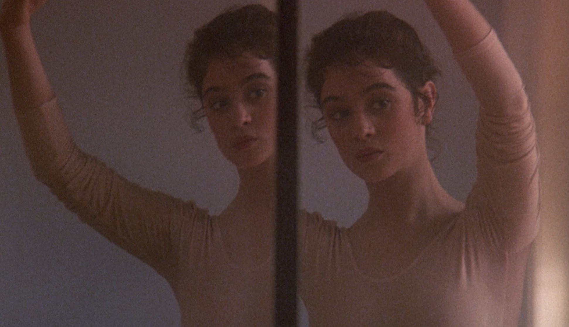 Actor Moira Kelly looks at two of her reflections and wears a light pink leotard.