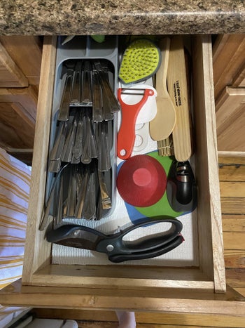 the same kitchen drawer with silverware filed into a slim organizer taking up less than half the room of the previous organizer and with plenty of room to see other tools inside