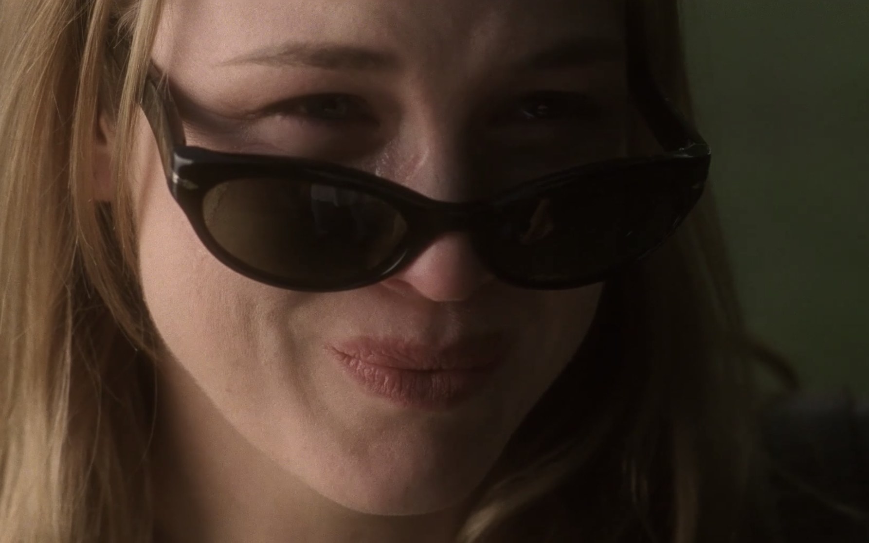 Close-up of actor Renée Zellweger smiles. Her sunglasses are edged down to her nose and she has tears in her eyes.