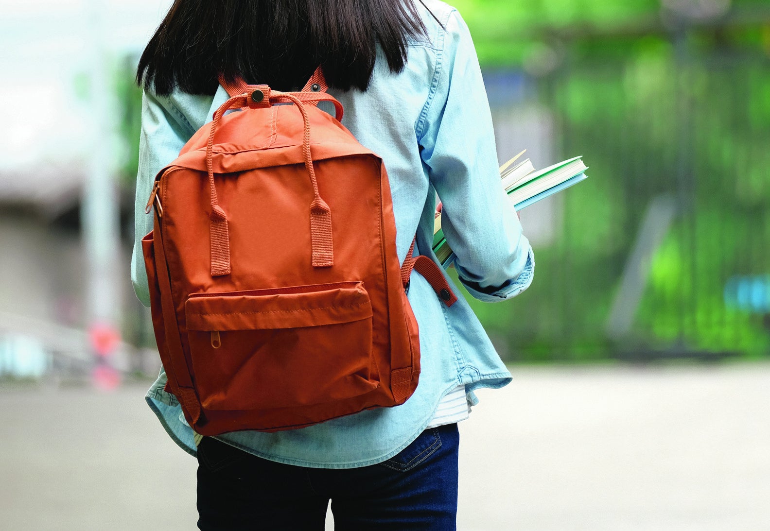 An Asian student stands alone, wearing their backpack and holding books