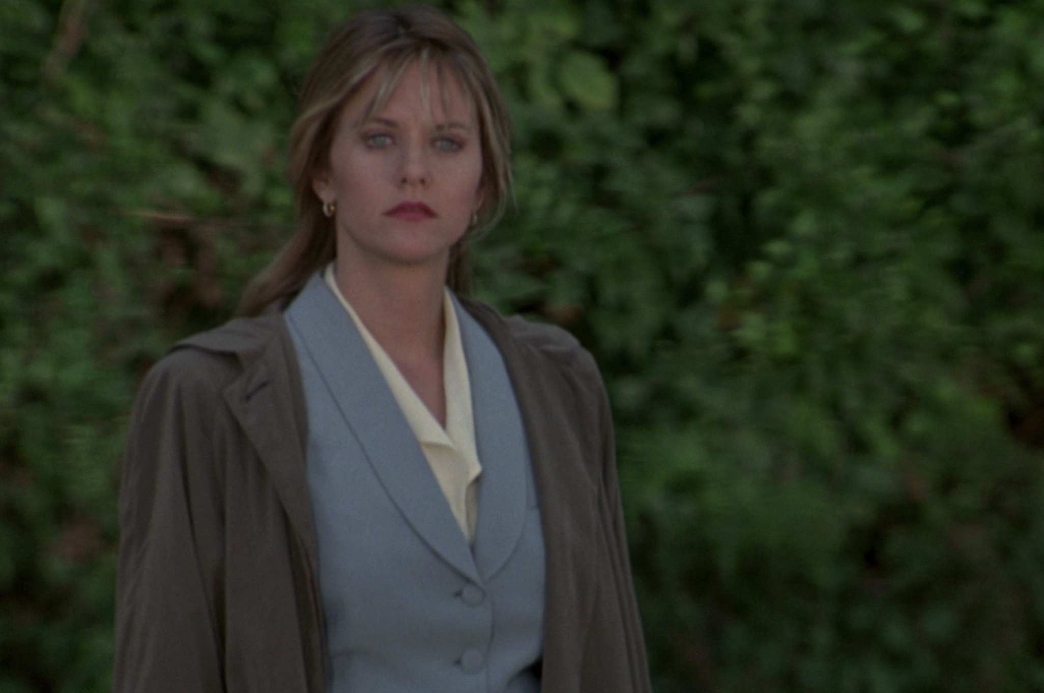 Actor Meg Ryan stands before a bunch of trees looking stunned.