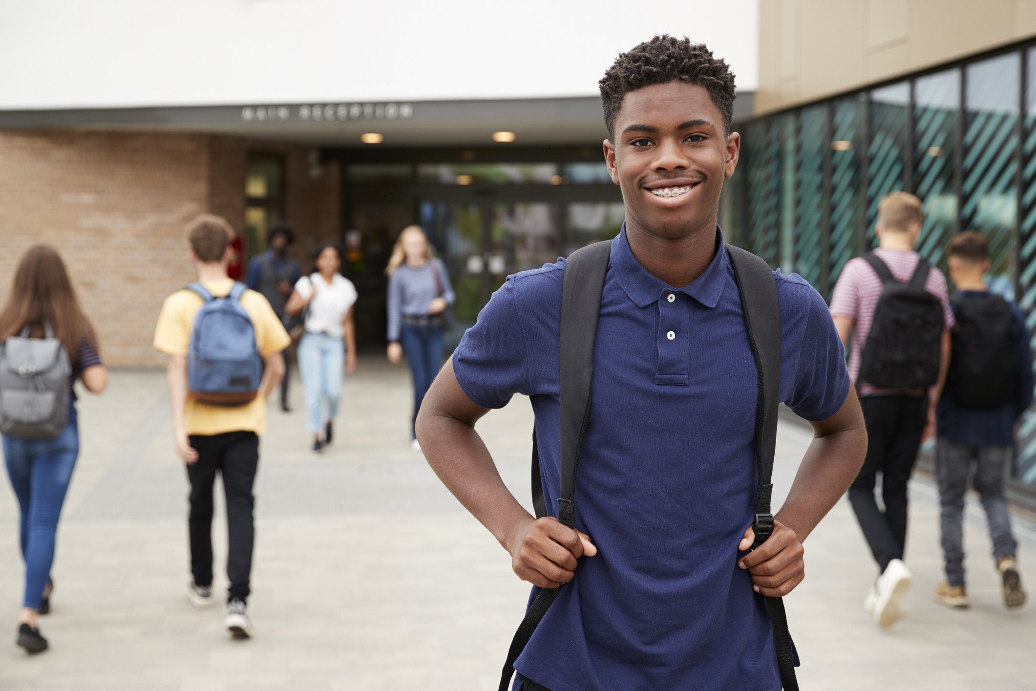 Happy teen boy in front of a school with a backpack on.
