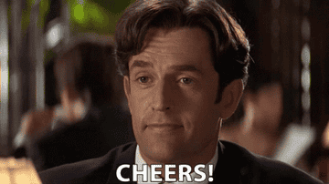 GIF of Actor Rupert Everett raising a class and says cheers in a scene from My Best Friend&#x27;s Wedding.