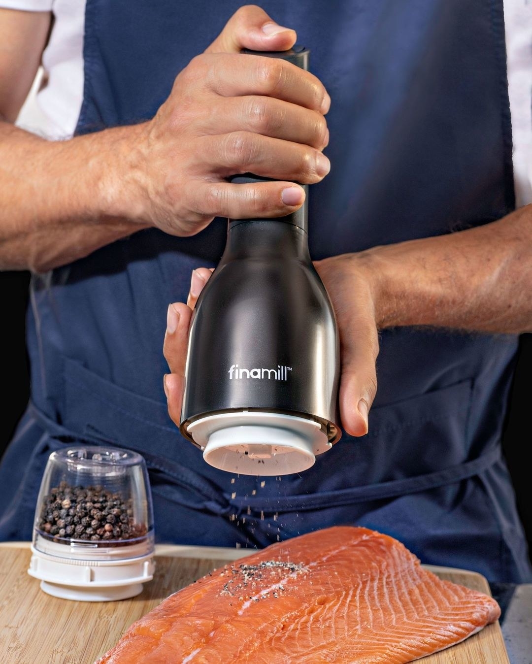 someone grinding spices onto a salmon filet