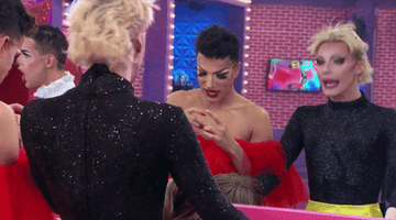 two drag queens half out of drag looking into the mirror