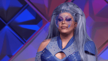 drag queen in blue futuristic look holding a finger up.
