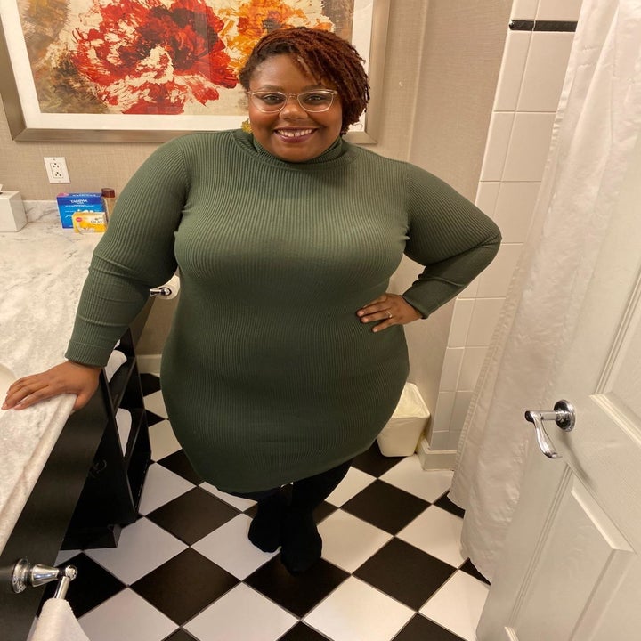 a reviewer poses in the olive dress styled with black stockings