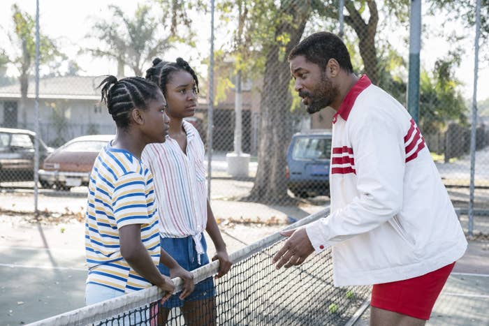 Demi Singleton as Serena Williams, Saniyya Sidney as Venus Williams, and Will Smith as Richard Williams, standing on a tennis court in Compton, California