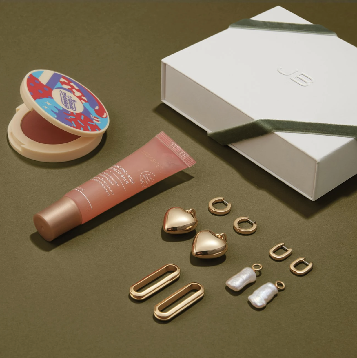 the jenny bird gift set arranged neatly on a simple backdrop; the items included a lip balm, a blush, and two pairs of customizable earrings