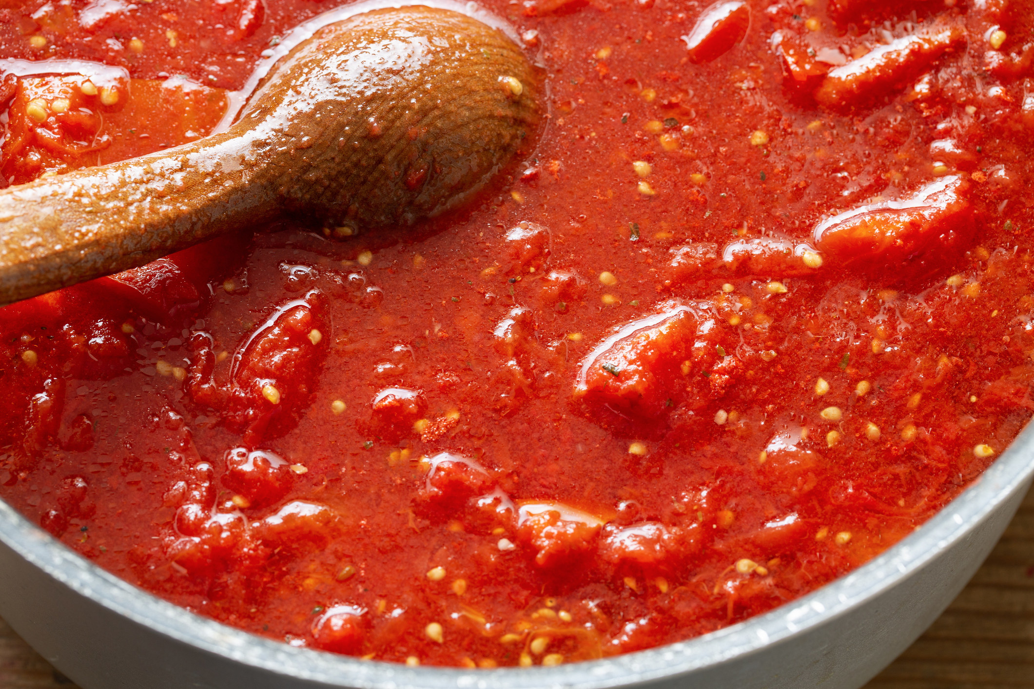 A wooden spoon in a pot of tomato sauce.