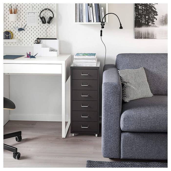 A black Ikea drawer unit next to a sofa and a desk