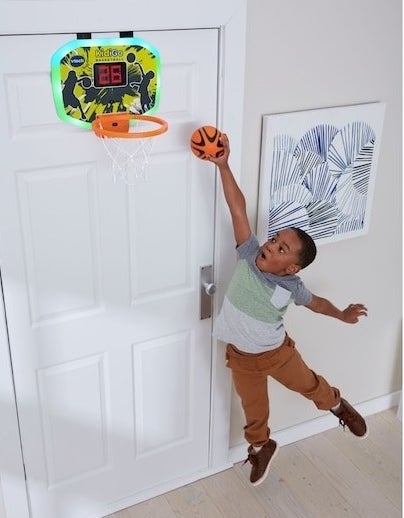 a child leaping to score a small basketball into a net that is hanging over a door