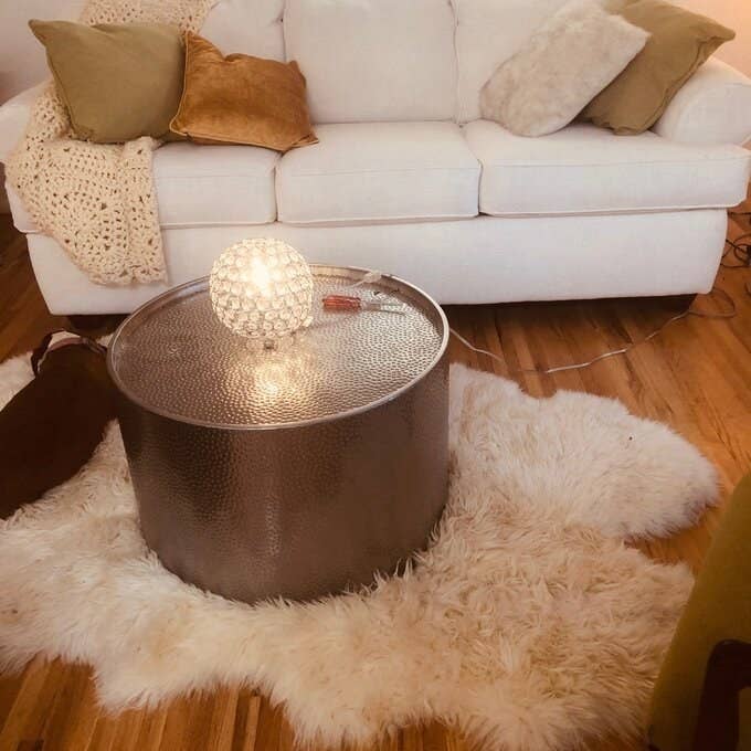 the gold drum coffee table on a white shag carpet with a gold ball on top of it and a couch behind it