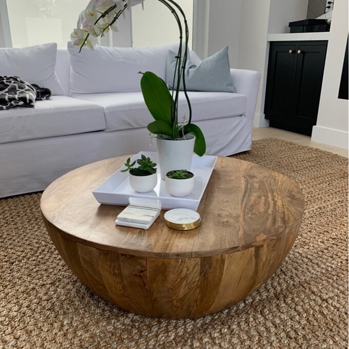 the round wood table with a white tray and potted plants on top and a white couch behind it