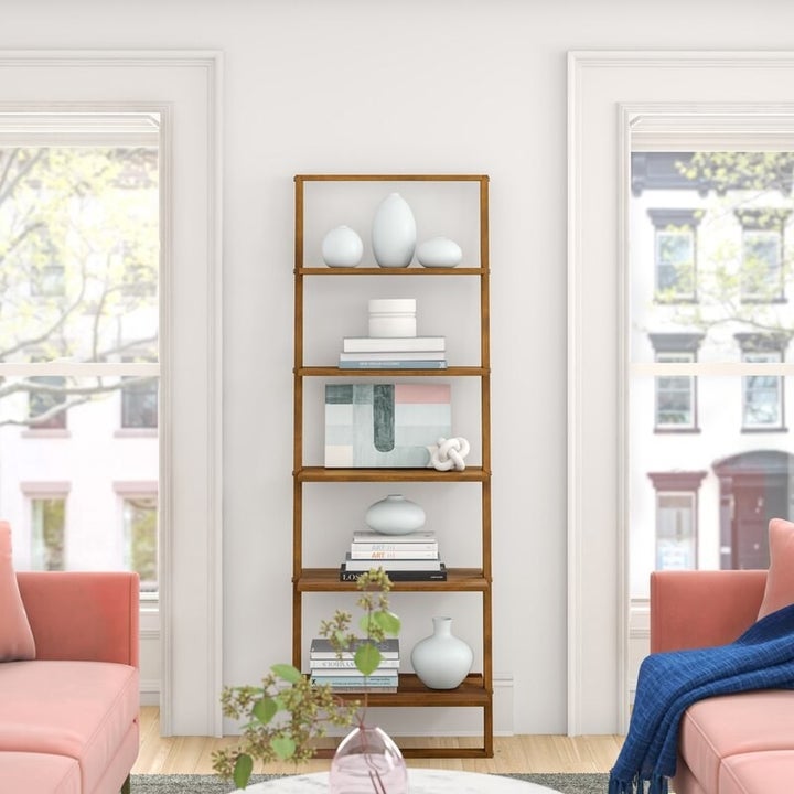 the brown bookcase against a white wall with books and vases on each shelf and two pink couches in front of it