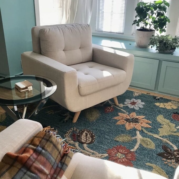 the chair in cream on a floral rug with a glass table next to it