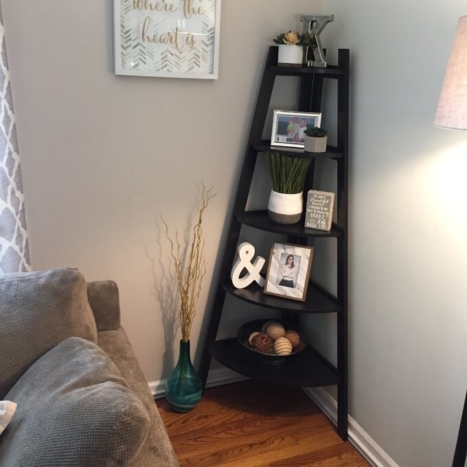 the black corner bookcase with decorations on the shelves including pictures, trinkets, and plants