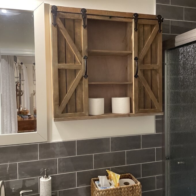the brown wall cabinet with two rolls of toilet paper in it hanging next to a mirror