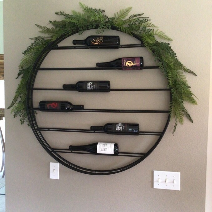 the round wine rack on the wall with six bottles of wine in it and a half wreath around the top