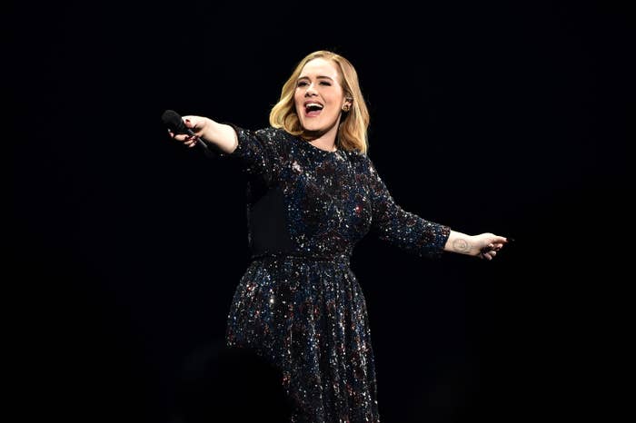 Adele extends her arms while holding a microphone
