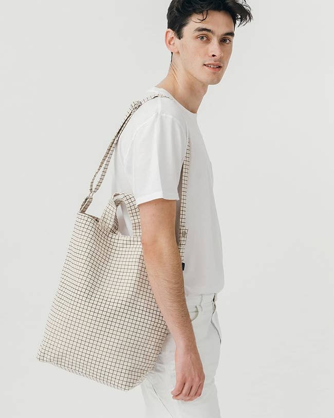 model wearing the tote bag over their shoulder that also has short handles in white with black grid pattern