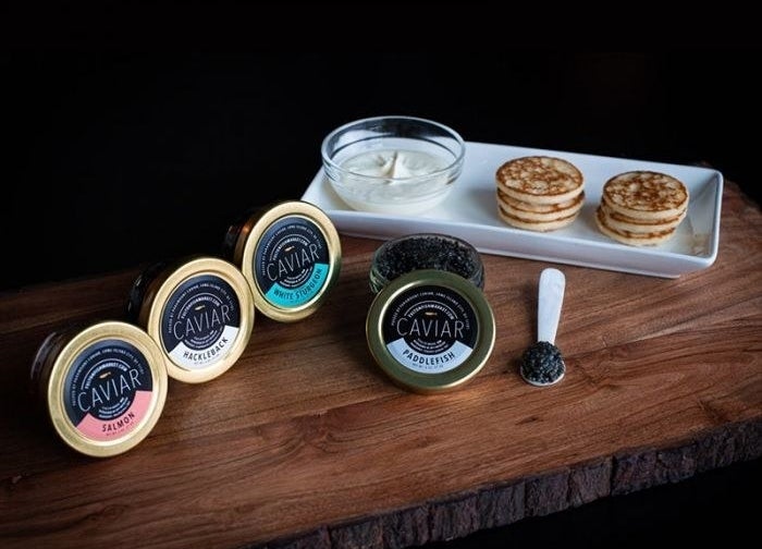 four tins of caviar, a mother of pearl spoon filled with roe, several blinis, and a serving of creme fresh
