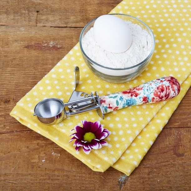 The cookie dropper with a floral handle set beside a bowl of flower and dish towel.