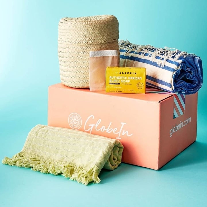 a box that says "GlobeIn" surrounded by two woven towels, a tan basket and a bar of African Black soap