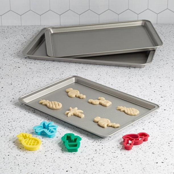 A cookie sheet with cookie dough on it and four cookie cutters beside it.