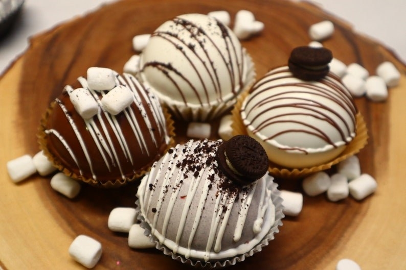 four hot cocoa bombs with marshmallows tiny oreos and drizzle design on them