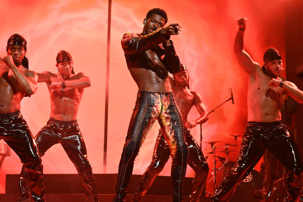 Lil Nas performs onstage in leather pants with a flame motif as he&#x27;s surrounded by backup dancers