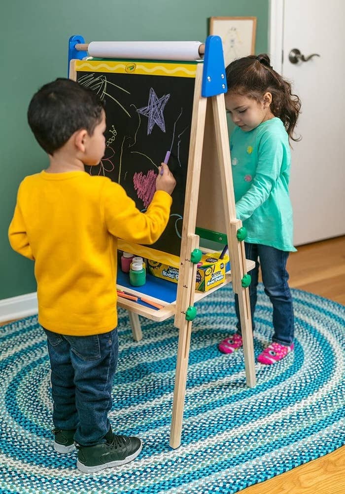 Two kids playing on either side of a wooden easel
