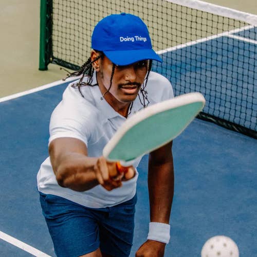 a model hitting a ball with a paddle while wearing the hat