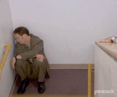 Dwight from the office looking sad and sitting in a corner in the hall