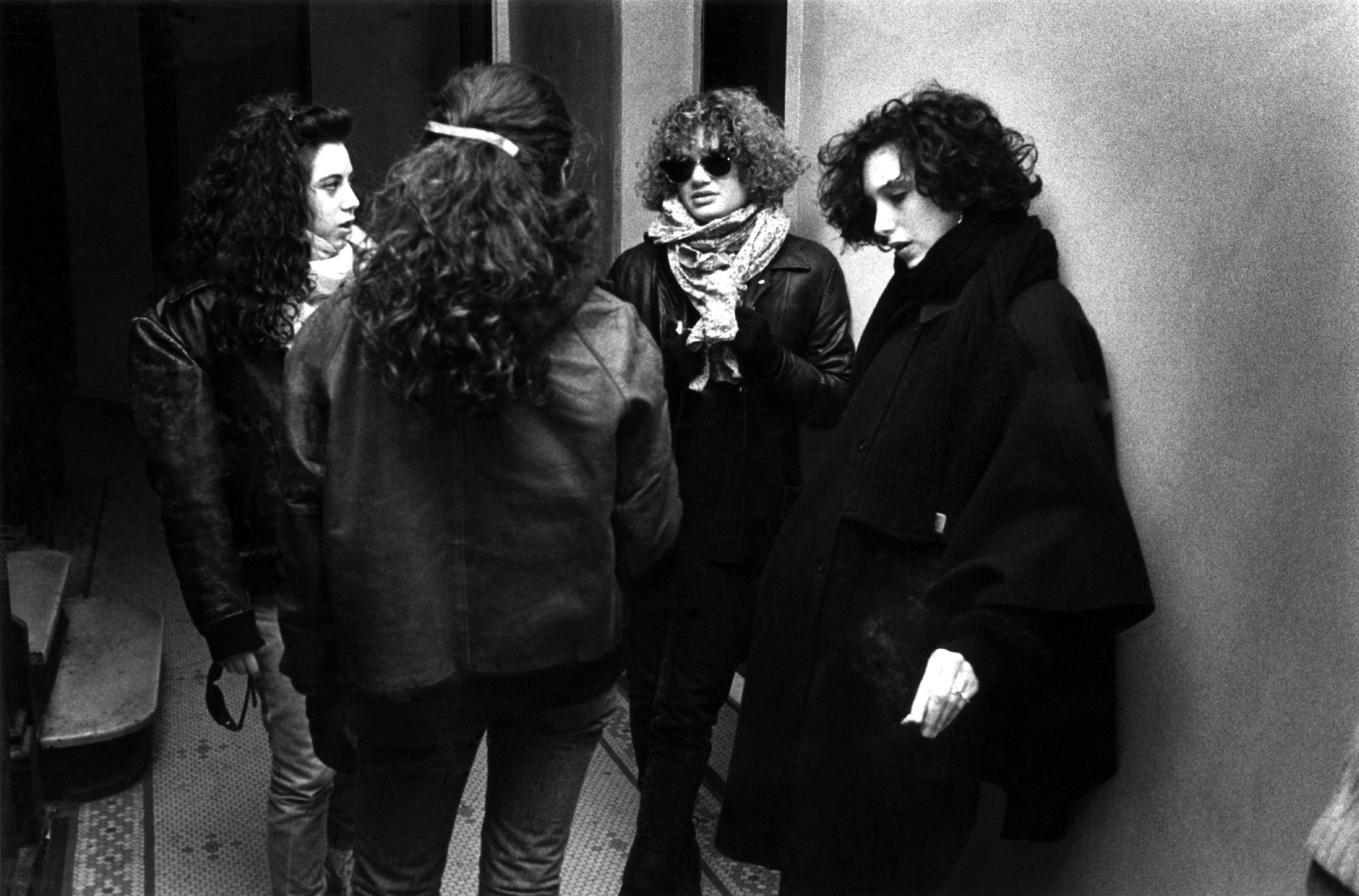 Four curly haired girls in coats in a stairwell in a new york city building