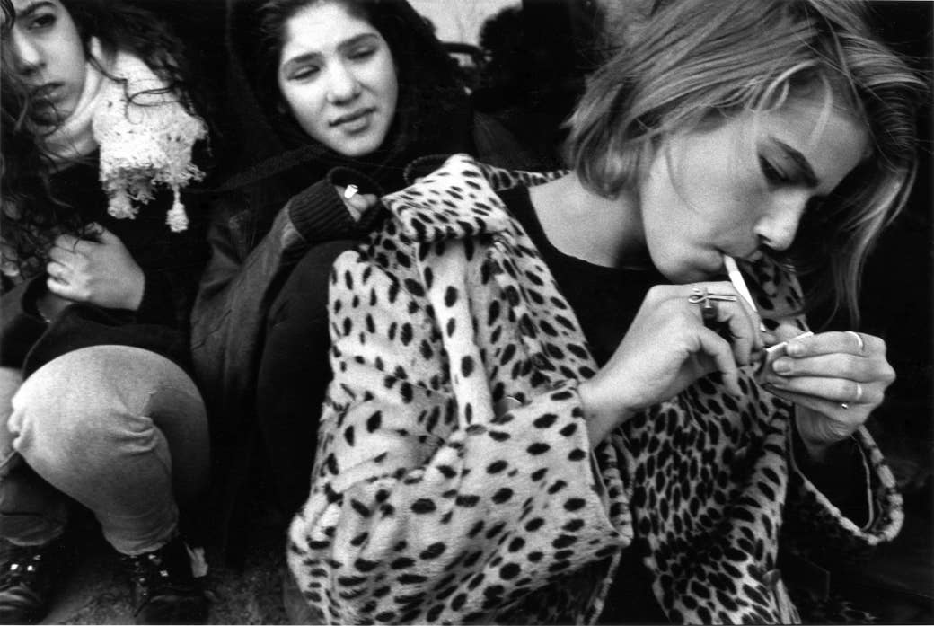 A girl lights a cigarette while her friends crowd around her 