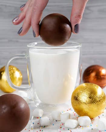 round hot chocolate bomb being dropped into a glass of hot milk