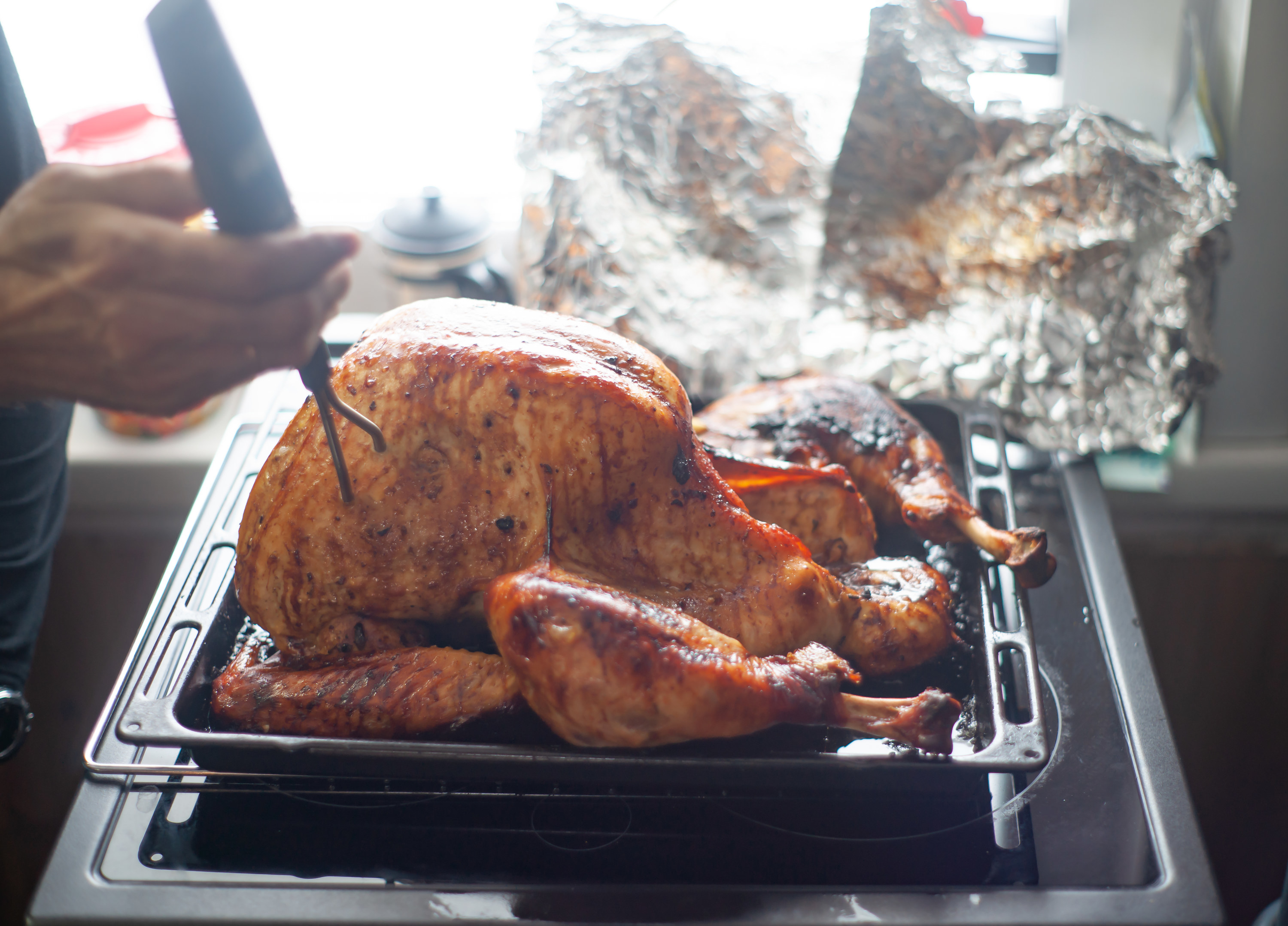 Roasted turkey in roasting pan, next to a tent of aluminum foil.