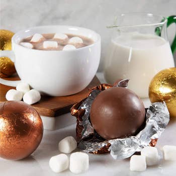 wrapped and unwrapped chocolate bombs in front of hot chocolate full of marshmallows