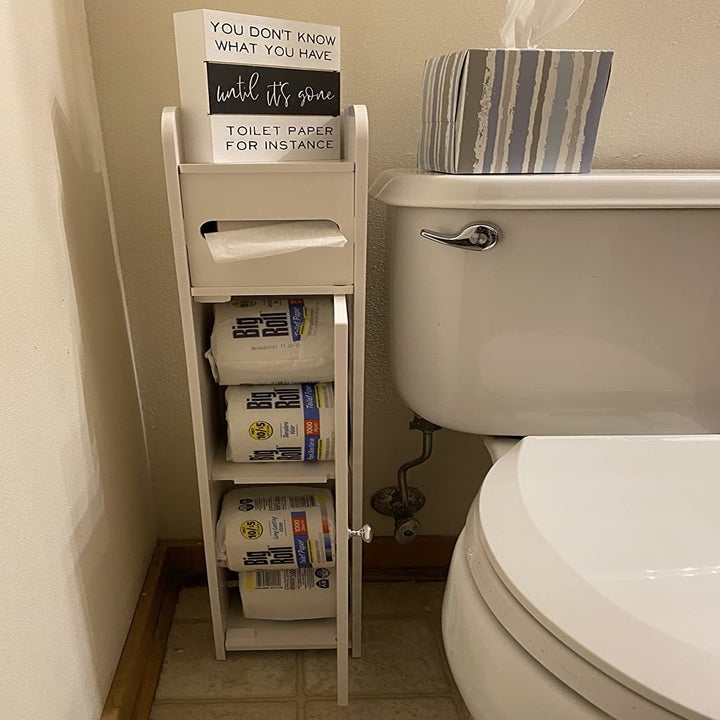 a reviewer photo of the cabinet open and filled with extra rolls of toilet paper