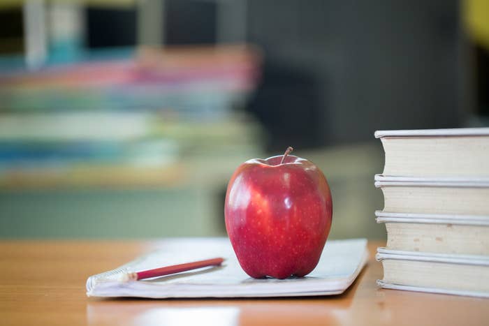 A school teacher&#x27;s desk with stack of books and apple