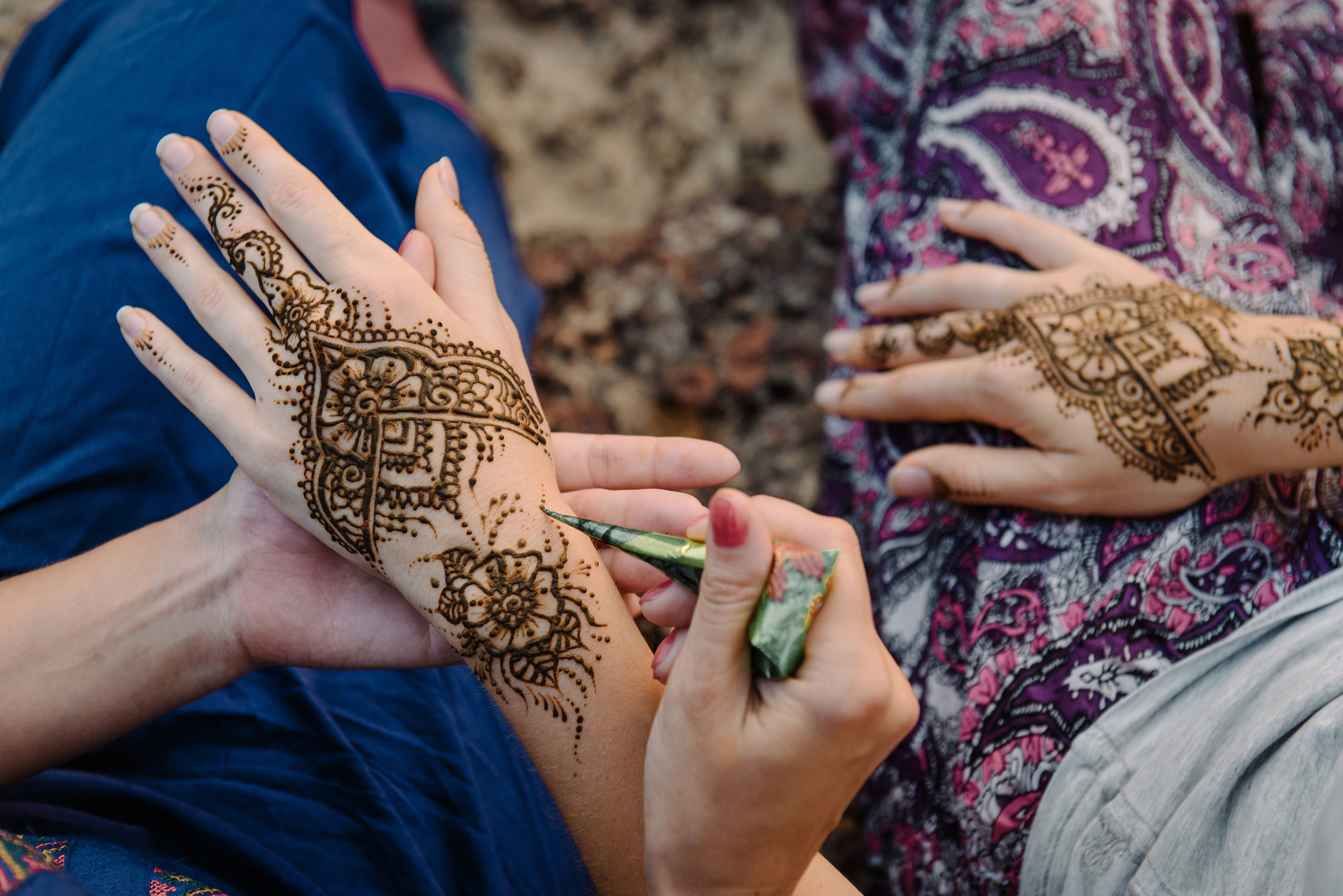 A woman applying henna to another person sitting beside her