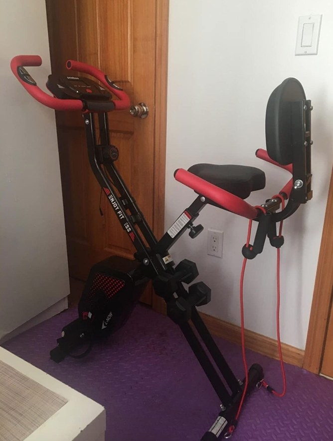 black exercise bike with red handle bars, dumbbell attachment, and red resistance bands on back of seat